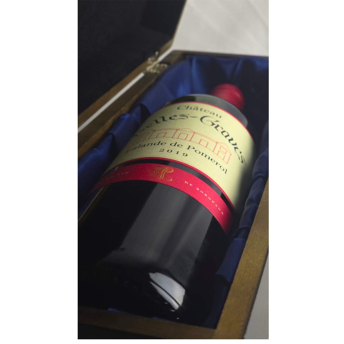Close-up of Château Belles-Graves 2019 bottle resting on the blue silk lining inside the elm wood gift box
